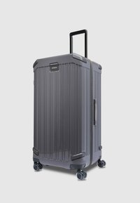 Grauer Hartschalenkoffer mit vertikalen Rillen, ausziehbarem Griff, vier Spinner-Rollen und abgerundeten Kanten. Verfügt über ein Etikett auf der Vorderseite.