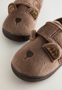 Chaussons en tissu marron avec une texture douce, ornés d'accents d'oreilles d'animaux, d'un nez brodé et d'une sangle en Velcro pour la fermeture.