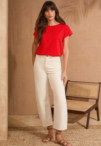 Top rojo de manga corta combinado con jeans de pierna ancha color crema. Textura de fibras naturales y contraste de colores claros. Sandalias marrones con tiras completan el look.