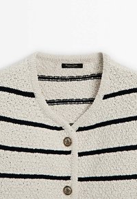 Gilet en tricot crème avec des rayures horizontales bleu marine et noires, doté d'un col en V et de deux boutons ronds métalliques à l'avant.