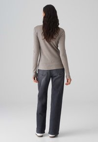 Hellebraunes Langarmshirt mit taillierter Passform, kombiniert mit dunkelgrauen weiten Jeans und weißen Sneakers. Glatte Stoffoberfläche.