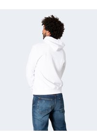 Felpa bianca con cappuccio realizzata in tessuto morbido, con tasca a marsupio, indossata con jeans in denim blu. Presenta una vestibilità rilassata e polsini a costine.