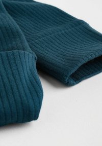 Indumento a maglia a coste color teal con una texture morbida, dotato di polsini arrotolati e una vista ravvicinata che mette in evidenza i dettagli del tessuto e la forma.