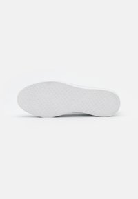Weiße Sneaker-Sohle mit einer strukturierten Oberfläche, die geprägte Markenlogos und geometrische Muster für Grip und Traktion aufweist. Abgerundete Form.