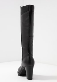 Bota negra hasta la rodilla hecha de cuero liso con un tacón grueso, que presenta un panel elástico en contraste en la parte superior y detalles de costuras.