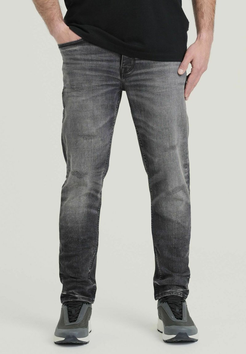 Vervaagde grijze jeans met een slim fit, voorzien van lichte slijtage. Gecombineerd met grijze sportschoenen met zwarte accenten en een zwart t-shirt.