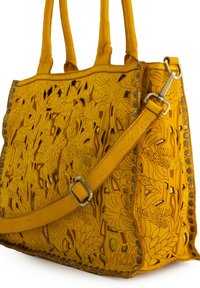 Yellow leather tote bag with intricate floral cutout design, studded accents along the edges, top handles, and a detachable shoulder strap.