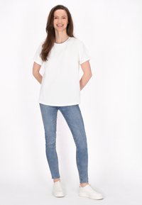 Hvid kortærmet t-shirt med opkrøllede ærmer, parret med lyseblå skinny jeans og hvide sneakers. Enkel, afslappet påklædning, minimal design.