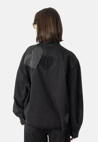 Svart denimskjorte med lange ermer, med hjerteformede lapper i forskjellige nyanser på baksiden. Avslappet passform og knappedetaljer.