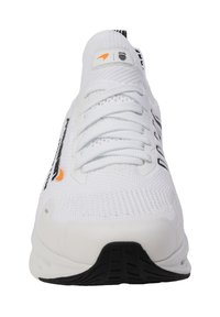 Baskets blanches de sport avec un dessus en maille texturée, logo noir et accents réfléchissants. Comprend des lacets, une semelle rembourrée et une semelle en caoutchouc noir.