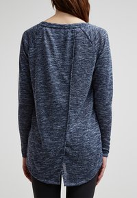 T-shirt à manches longues bleu marine avec une texture chinée, une finition arrondie et une fente au dos pour un détail supplémentaire. Le tissu semble doux et confortable.