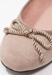 Ballerine plate en daim beige clair avec un nœud en satin torsadé et une bordure élastiquée autour de l'ouverture.