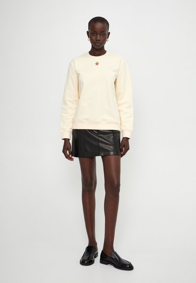 Creme sweatshirt med et broderet logo, parret med en sort læder mini-skjorte og sorte loafers. Glatte teksturer og tætsiddende former.