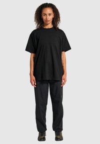 Czarna bawełniana koszulka z krótkim rękawem i okrągłym dekoltem, zestawiona z czarnymi spodniami w paski i ciemnymi butami. Prosty, luźny krój.