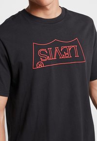 Camiseta de algodón negra con un gran logo rojo de Levi's impreso en el frente. Cuello redondo y mangas cortas con un ajuste relajado.