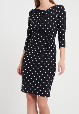 Zwarte jurk met witte polka dots, driekwart mouwen, gedrapeerde halslijn en een gedraaide plooidetail ter hoogte van de taille. Glad textuur van de stof.