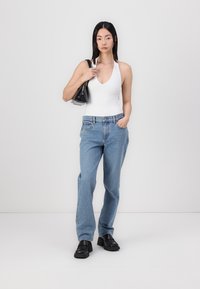 Bodysuit sans manches blanc, jeans droits bleu clair, chaussures à talons noires, tenant un sac à main noir. Textures lisses, design décontracté.