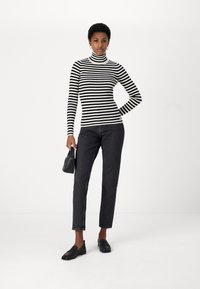 Maglione a righe bianche e nere a maniche lunghe, design aderente; abbinato a jeans scuri e mocassini neri. Gli accessori includono una piccola borsa nera.