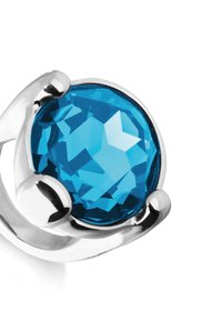 Bague en argent ornée d'une grande pierre précieuse bleue ronde et facettée, conçue avec des accents métalliques courbes autour de la pierre, reflétant la lumière.