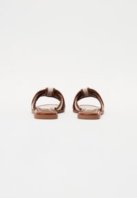Brune slide sandaler med brede, buede remme og en flad sål. Den teksturerede fodseng og accentremmen skaber et lagdelt design.
