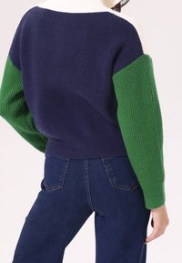 Suéter de punto con un cuello alto, con paneles en azul marino, verde y blanco; textura acanalada; combinado con jeans de mezclilla oscura.