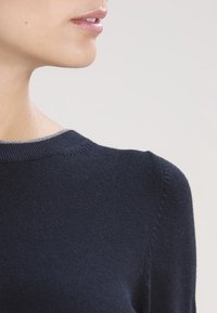 Mörkblå stickad tröja med rund halsringning. Har en fin struktur och kontrasterande ljusgrå kant vid kragen.