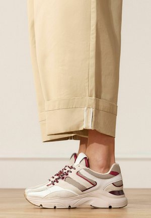 Beige and maroon mesh and suede sneakers worn with beige cuffed wide-leg pants on wooden floor.
