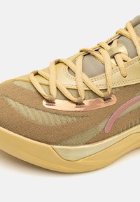 La scarpa presenta una toma superiore in tessuto giallo e marrone miscelato con lacci, una piastra decorativa metallica e una suola testurizzata per migliorare la presa.