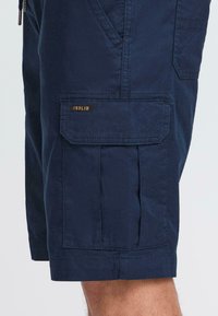 Mørkeblå cargoshorts laget av glatt stoff, med plisserte detaljer og sidelomme med logoetikett.