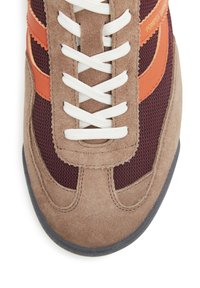 Zapatillas marrones y burdeos con un diseño de malla, acentos de ante, cordones blancos y detalles naranjas a lo largo de los laterales. Suela de goma.