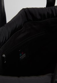 Intérieur d'un sac noir montrant une poche zippée et une étiquette en tissu avec un logo carré turquoise et rouge et le texte "even & odd".
