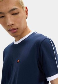 Camiseta azul marino con ribete y franjas laterales blancas. Presenta un pequeño logotipo bordado multicolor en el pecho. Textura de tejido suave.