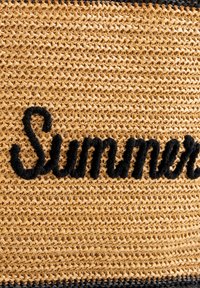 Woven straw bag in natural hues with black, plush lettering spelling "Summer." Features a textured, open weave design with a horizontal stripe.