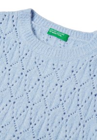 Un suéter de punto azul claro presenta un patrón texturizado con formas de diamantes y acentos en azul oscuro. Incluye una etiqueta verde que dice "United Colors of Benetton".