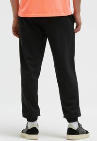 Schwarze Jogginghosen mit gerippten Bündchen, lockerem Schnitt und glatter Textur, kombiniert mit schwarzen und grauen Sneakers.