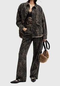 Conjunto de chaqueta de mezclilla y pantalones con estampado de leopardo negro y marrón, combinado con una blusa de encaje negra y un bolso de piel sintética color beige. Unas bailarinas negras completan el look.