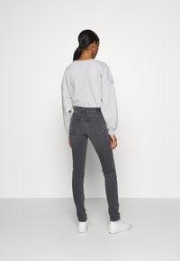 Sudadera gris con hombros caídos combinada con vaqueros ajustados de cintura alta en gris oscuro. El modelo lleva zapatillas blancas. Diseño sencillo, con detalles mínimos.