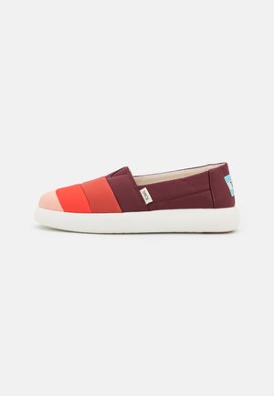 Slip-on sko med polstrede stofbånd i pink, rød og bordeaux, hvid sål og et lille TOMS-mærkat på siden.