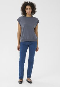 Grå kortærmet sweater med afslappet pasform og ribbet kant, parret med blå lige ben jeans. Modellen bærer sorte flade sko.
