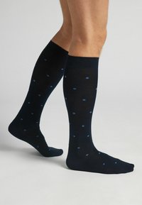 Knief hohe Socken in Marineblau mit hellblauen Punkten, aus einem glatten, dehnbaren Material. Gerippter Bund für einen sicheren Sitz.