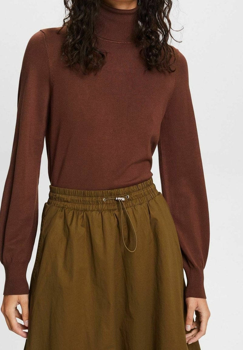 Pull à col roulé marron associé à une jupe ample vert olive avec une taille élastique et un cordon de serrage.