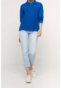 Niebieska koszulka polo z długim rękawem i kołnierzykiem, z małym logo. Połączona z jasnoniebieskimi, skróconymi dżinsami i białymi trampkami.