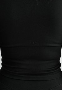 Débardeur noir à côtes avec un design sans couture et un logo de marque subtil à l'ourlet, fabriqué en tissu extensible et respirant.