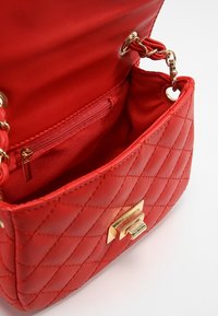 Borsa a tracolla rossa trapuntata in materiale sintetico con un clasp color oro, dotata di una tasca interna e di un rivestimento liscio e testurizzato.