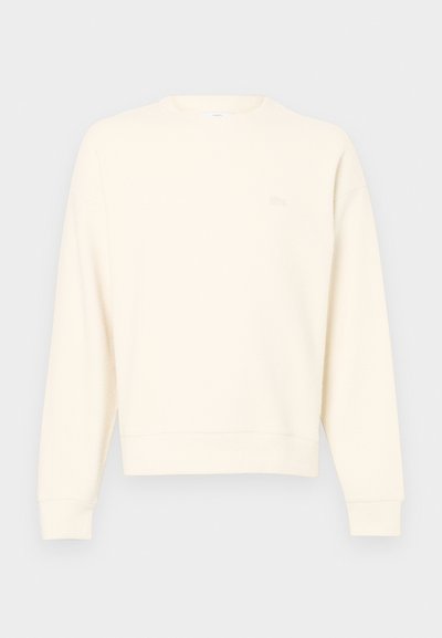 Sweatshirt beige clair en tissu texturé, avec un col rond, des manches longues et un logo subtile sur la poitrine.