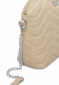 Beige prošívaná kabelka vyrobená z texturovaného syntetického materiálu. Má stříbrný řetízkový popruh a zipové uzavření s malým logem.