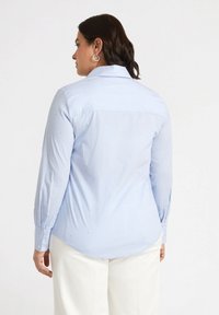 Camicia a righe azzurro chiaro con maniche lunghe, decorazioni simili a perle, colletto a punta e orlo curvo. Vista posteriore mostrata.