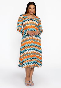 Langarmkleid mit einem mehrfarbigen Zickzackmuster in Orange, Blau und Weiß sowie einem Schlüsselnausschnitt-Detail.