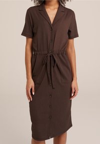 Brun kortärmad klänning i strukturerad tyg, knäppning fram och knytmidja. Har två sidofickor och en medellång längd.