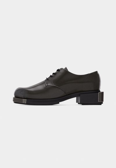 Black leather lace-up dress shoe with squared metal toe cap and block heel featuring metal accents on plain background.